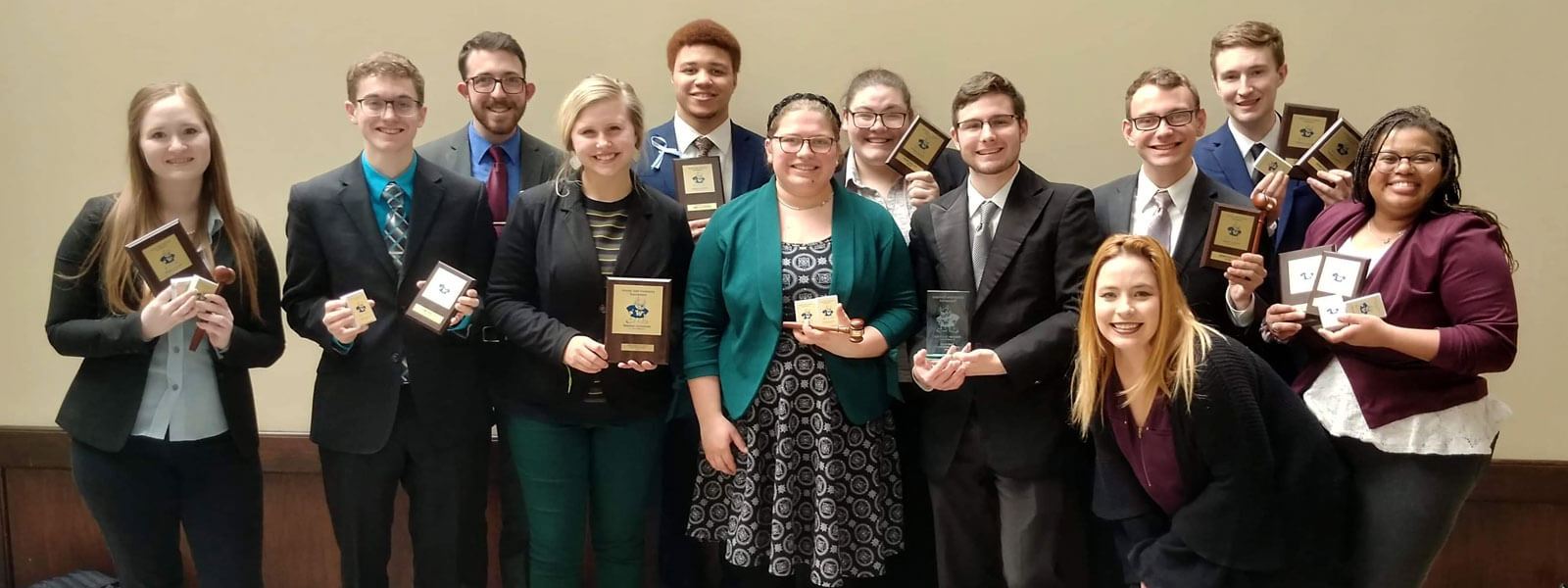 speech and debate team members pose with handfuls of trophies