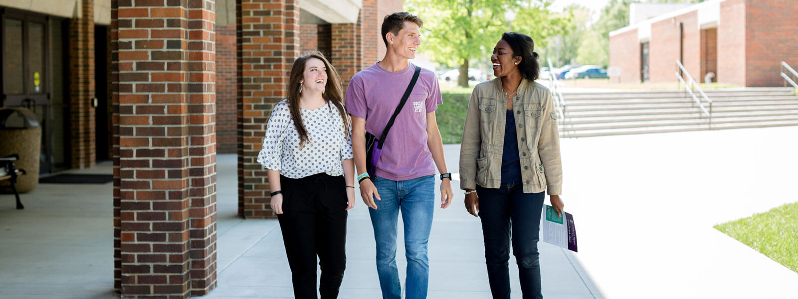 three students walking on sidewalk on campus
