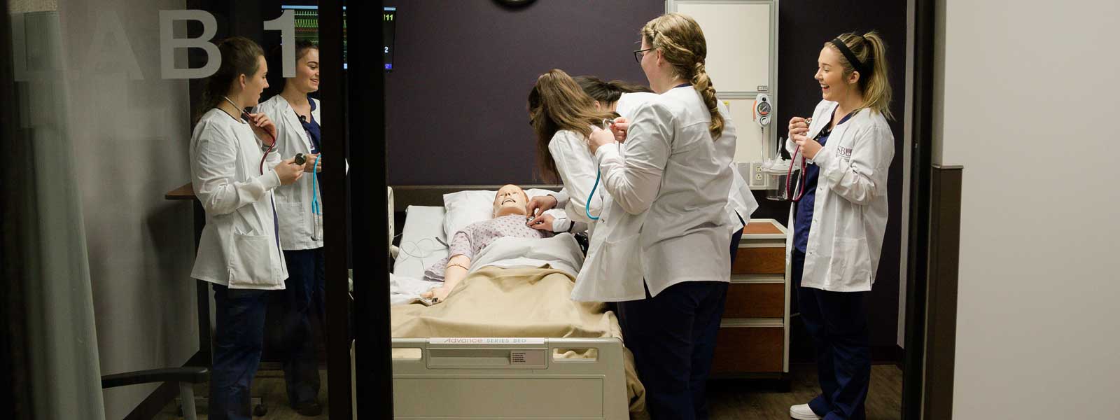 group of nursing students in simulation lab practicing listening to mannequin's heartbeat