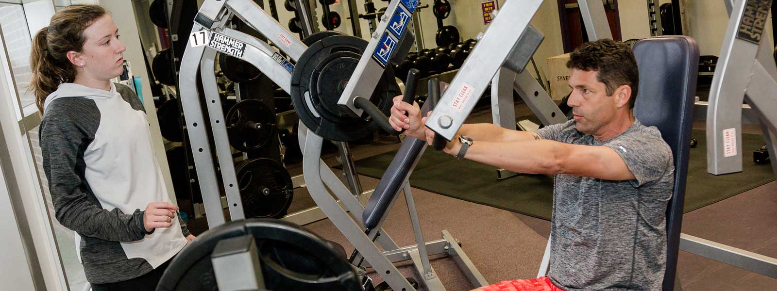 female personal trainer observes as male adult uses exercise equipment