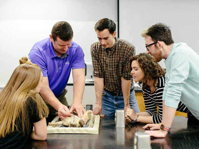 Professor and students gathered around anatomy mannequin