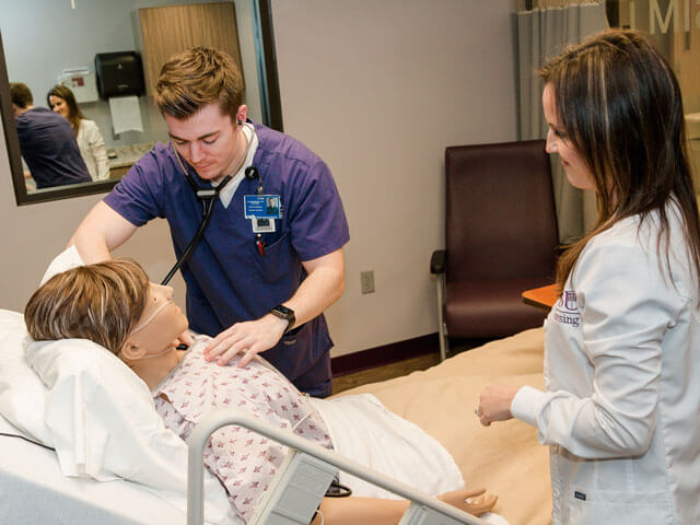 nursing student practices with mannequin with instructor looking on