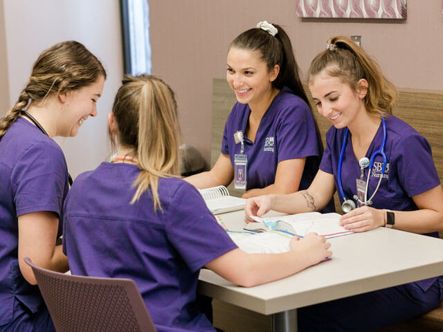 SBU students smiling as they study at a table